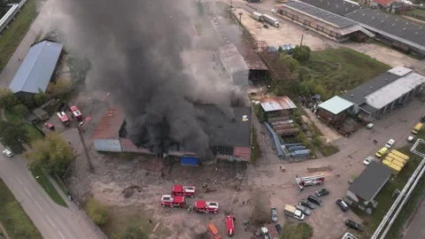 Aerial view of massive industrial fire with thick black smoke and fire trucks Stock Footage 321362706