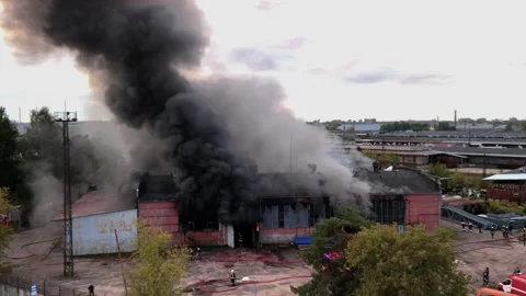 Aerial view of massive industrial fire with thick black smoke and fire trucks Stock Footage 321362744