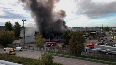 Aerial view of massive industrial fire with thick black smoke and fire trucks Stock Footage 321362758