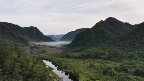 Aerial view of a misty valley surrounded by lush green hills, tropical forests Stock Footage 346012217