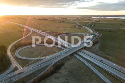 Aerial view of modern highway road intersection at dawn on raising sun backgr Stock Photos