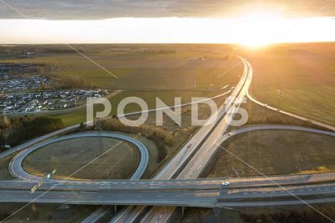Aerial view of modern highway road intersection at dawn on raising sun backgr Stock Photos