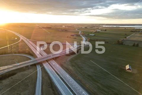 Aerial view of modern highway road intersection at dawn on raising sun backgr Stock Photos