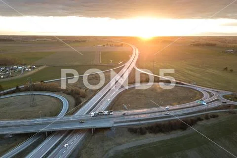 Aerial view of modern highway road intersection at dawn on raising sun backgr Stock Photos