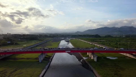 Aerial View of a Modern Red Arch Bridge Spanning Over a Tropical River Stock Footage 334730127