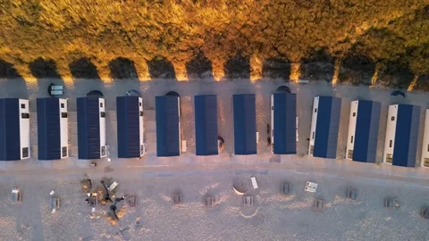 Aerial view of modular beach cabins aligned along a sandy shore, backed Video stock 326792289