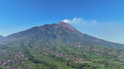 Aerial view of Mount Merapi volcano emitting smoke above lush green farmland Stock Footage 315289246