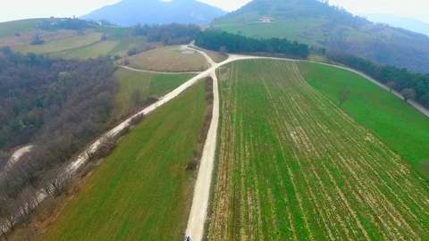 Aerial view of a mountain biker pedaling on a dirt road among the green hills. Stock Footage 91711684