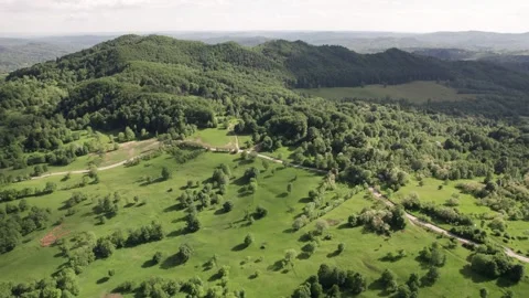 Aerial view of a mountain meadow over forests and a distant village in Romania Stock Footage 336493381