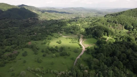 Aerial view of a mountain meadow over forests and a distant village in Romania Stock Footage 336493389