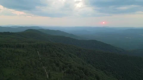 Aerial view of mountain ridges under dramatic clouds with the red sun setting on Stock Footage 319007094