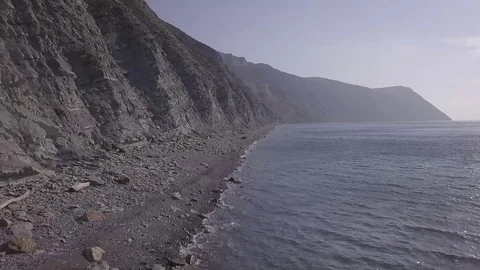Aerial view moving along the cliffs near the sea above stones at the beach Stock Footage 86902590