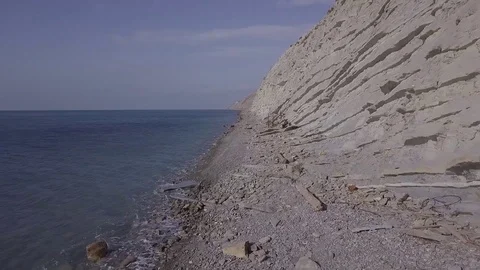 Aerial view moving along the cliffs near the sea above stones at the beach Stock Footage 86902595
