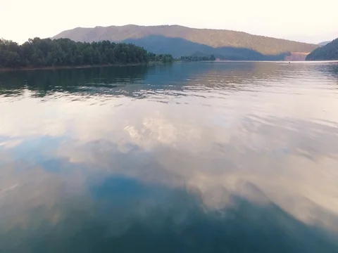 Aerial view moving fast over calm water, pan up to island and cliffs Stock Footage 77685720