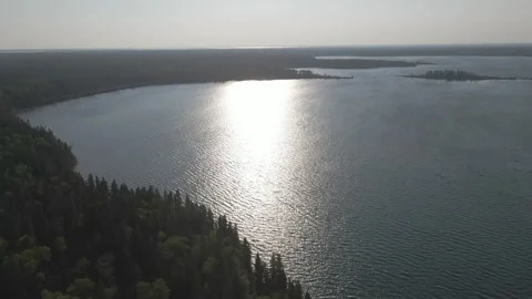 Aerial view moving forward over a large lake surrounded by a boreal forest Vídeos de archivo 256032209