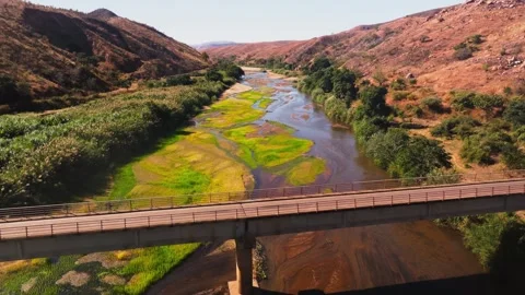Aerial view moving towards a bridge over a river with lush green vegetation on 스톡 동영상 308394352
