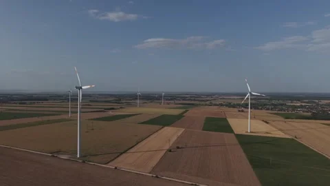 An aerial view of multiple wind turbines standing across a vast patchwork of Stock Footage 342774783