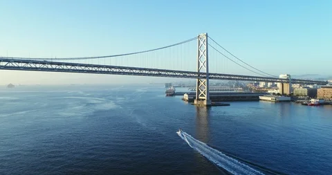 Aerial view of Oakland Bay Bridge at sunrise with boat driving under bridge Stock Footage