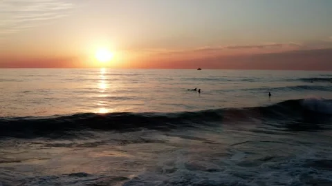 Aerial view to the ocean with calm waves during sunset with surfers on boar.. Stock Footage 303707276