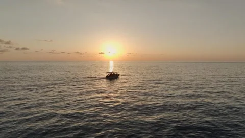 Aerial View: The ocean glows with sunset reflections as a small boat floats Stock-Footage 296079180