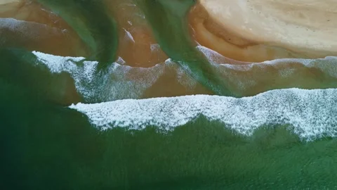 Aerial view of ocean waves breaking on a sandy beach with river water mixing in Stock Footage 318958298