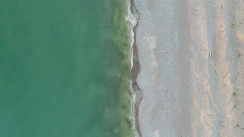 Aerial view of the ocean with waves crashing on a pebble beach Stock Footage