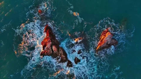 Aerial view of ocean waves crashing against dark volcanic rocks at sunset golden Stockbeeldmateriaal 342705701