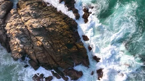 Aerial view of ocean waves crashing against jagged coastal rocks on a sunny day. Stockbeeldmateriaal 342788292