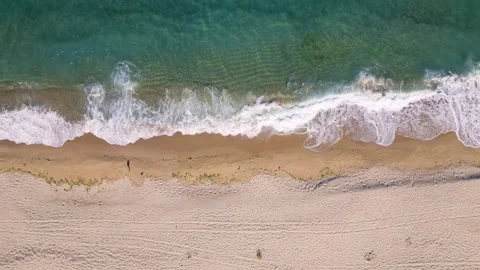 Aerial view of ocean waves gently rolling onto an empty sandy beach. Clear Stock Footage 317384206