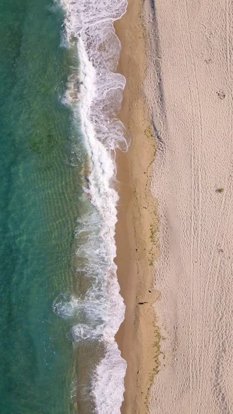 Aerial view of ocean waves gently rolling onto an empty sandy beach. Clear Stock Footage 317385049