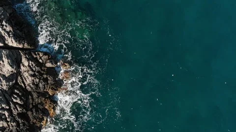 Aerial view of ocean waves hitting a rugged and cliffed coastline on a sunny day Vídeo Stock 331200262