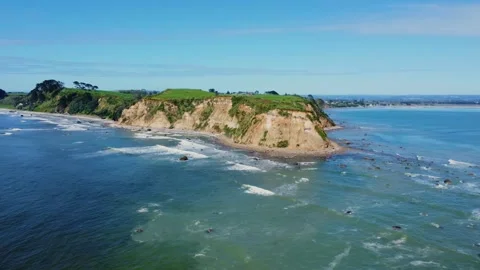 Aerial view of ocean waves hitting a green cliff coastline on a sunny day Stock Footage 344439930
