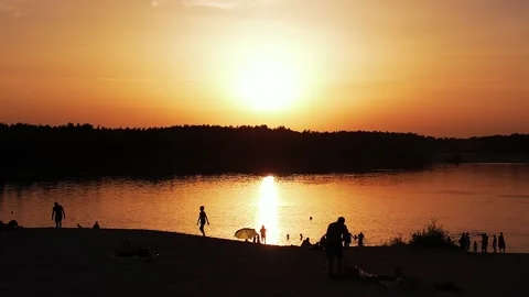 Aerial view of orange river surface at sunset and silhouettes of vacationers on Vidéo 224270414