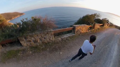 Aerial view, orbit around a man jogging on a scenic path on the cliff at sunset Stock Footage 107913154