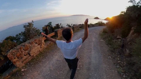 Aerial view, orbit around a man walking on a scenic path on the cliff at sunset Stock Footage 107919519