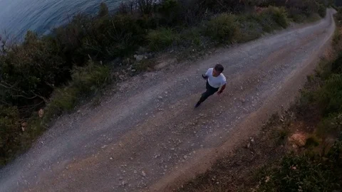 Aerial view, orbit around a man walking on a scenic path on the cliff at sunset Stock Footage 107921054