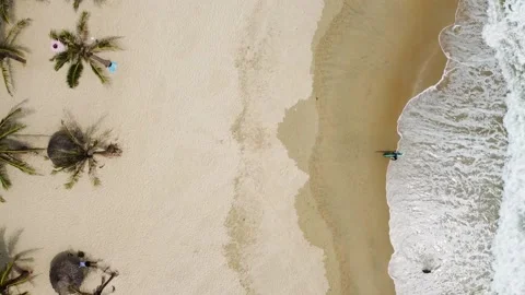 Aerial view over the beach with a surfer walking out from the water and waves Stock Footage 163365621