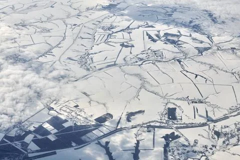 Aerial view over clouds top to snow covered rivers, fields and roads, winter  Stock Photos