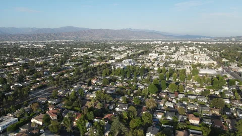 Aerial view over a leafy suburban valley with mountains behind Stock Footage 345547408