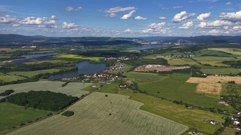 Aerial view over patchwork fields, village by lake under blue sky, tranquil Stock Footage 347914961