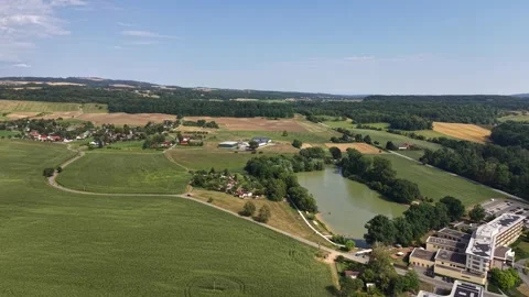 Aerial view over patchwork fields, village pond, and modern campus buildings Stock Footage 348504185