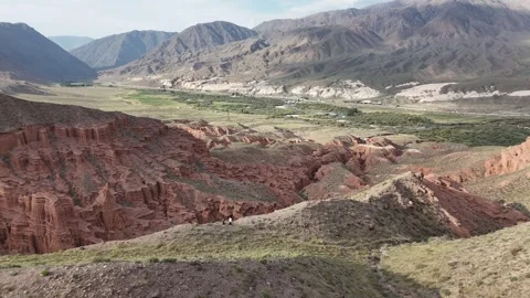 Aerial view over red eroded canyons and a green valley, Kyrgyzstan Видео 347239487