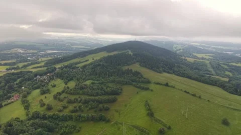 Aerial view over rolling green hills, patchwork fields, forests, and distant Stock Footage 347914973