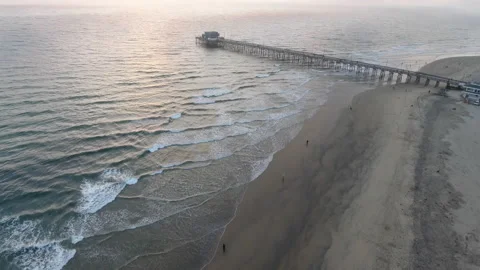 Aerial view over rolling waves along the coast at sunset by pier Stock Footage 157140514