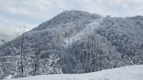 Aerial view over snowy mountain ridge valley with clouds, cable car lifting. Stock-Footage 101537357