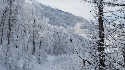 Aerial view over snowy mountain ridge valley with clouds, cable car lifting. 스톡 동영상 101537608