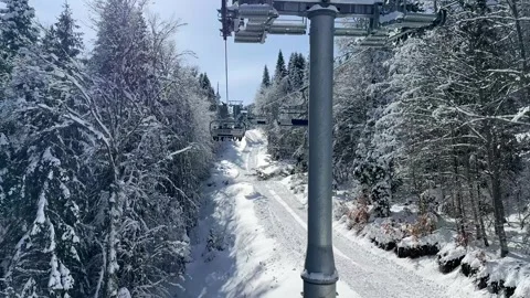Aerial view over snowy mountain winter forest with chair lift at ski resort. Stock Footage 329480409