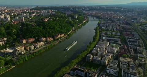 Aerial view over town at sunset along a blue river. A tourist ship moves along Stock-Footage 274492105