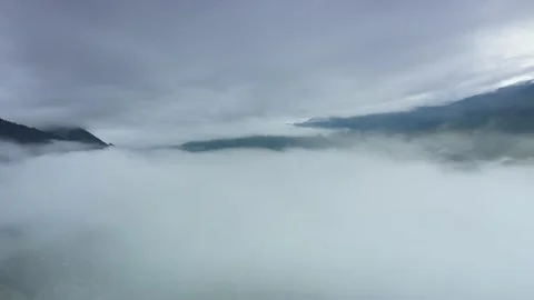 Aerial view over valley surrounded by mountains and covered with fog and mist Stock Footage 141522434