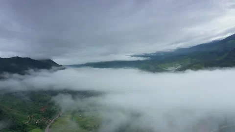 Aerial view over valley surrounded by mountains and covered with fog and mist Stock Footage 141522496
